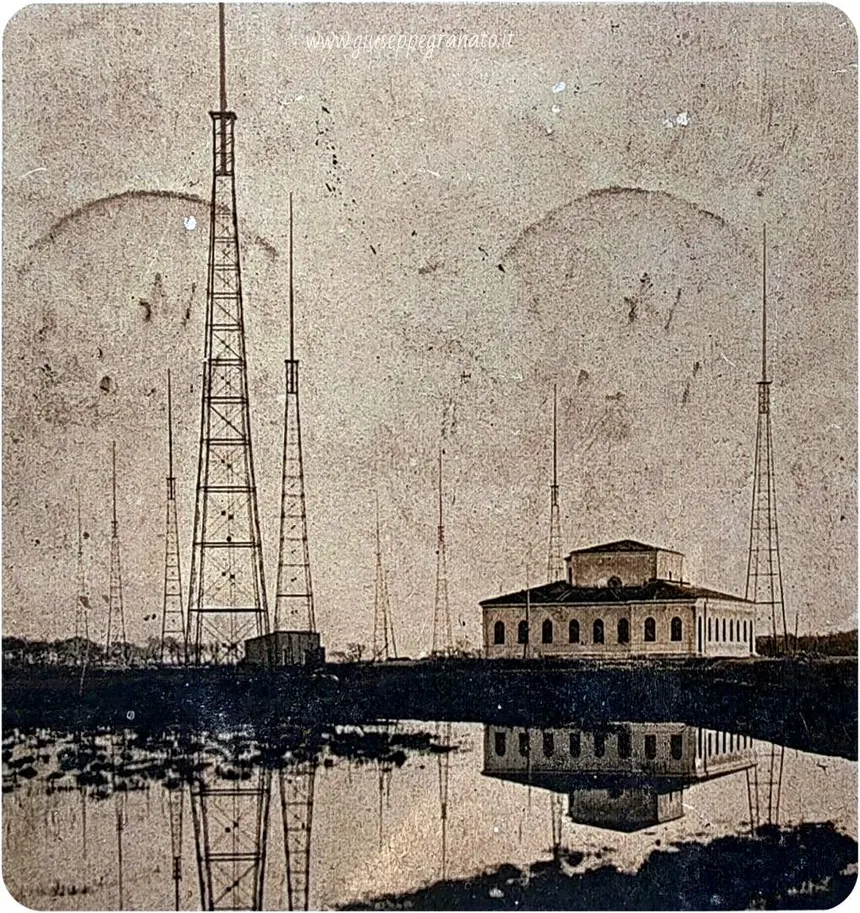 Foto storica della stazione radiotelegrafica di Coltano con antenne e edificio riflessi nell'acqua.